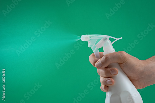 Canvas Print hand squeezing the trigger of a spray bottle spraying water mist on a green back