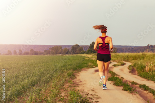 Sport girl running outdoor. Young woman running in field at evening. Back view running lass on meadow at sunset. Fitness training.