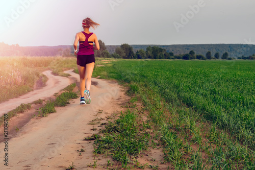 Athletic Blonde Teenage Girl Running At Dirt road In field. Sport girl running outdoor. Young woman running in field at evening.  © Konstantin
