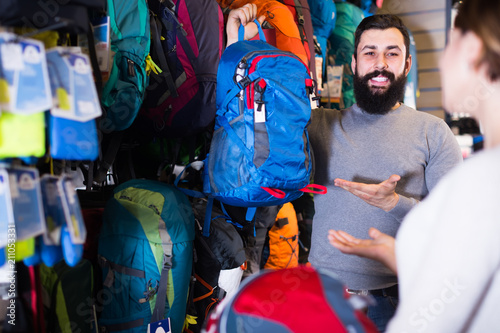 positive young pair examining rucksacks in sports equipment store