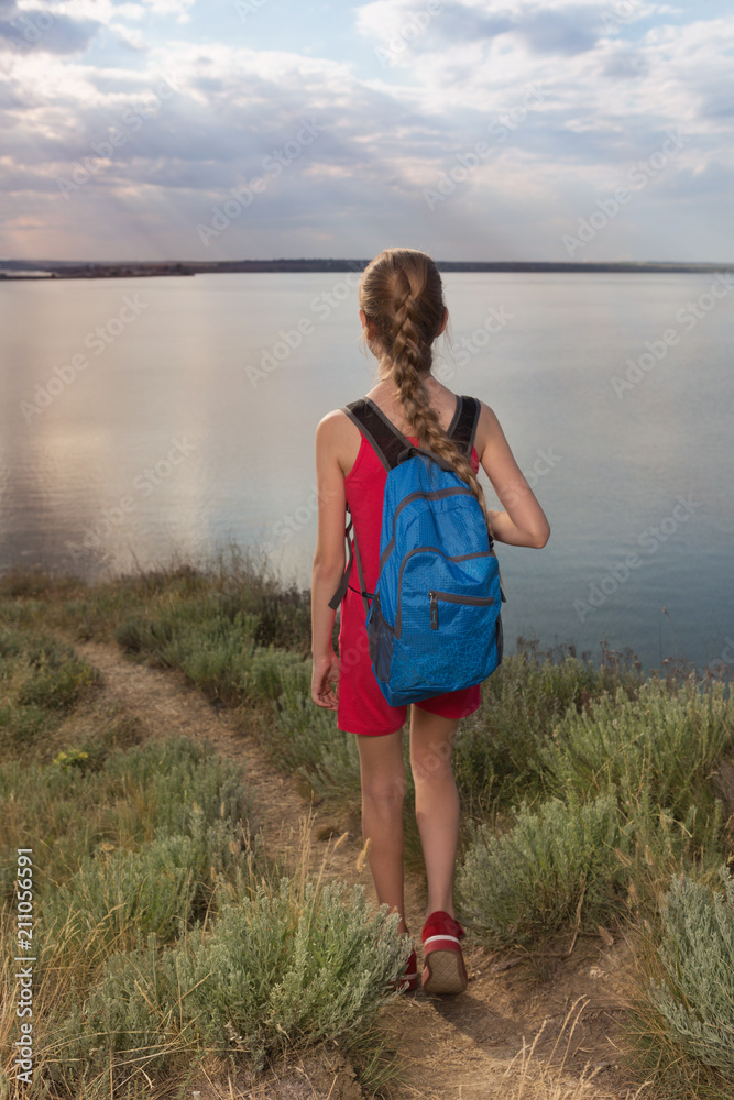 girl alone walks with ryuzak on the road, against the background of the sea or lake, evening journey, girl back to the camera, sunset girl alone walks with ryuzak on the road, against the background of the sea or lake, evening journey, girl back to the camera, sunset