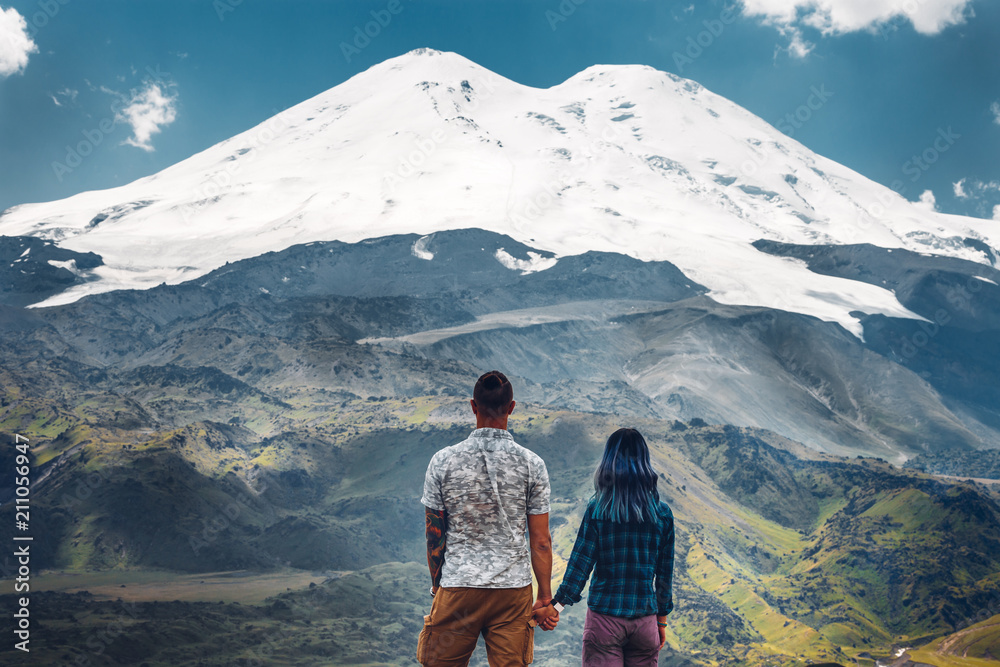Happy couple holding hands and enjoying the view of Mount Elbrus, rear view. Travel Holiday Destination Concept\