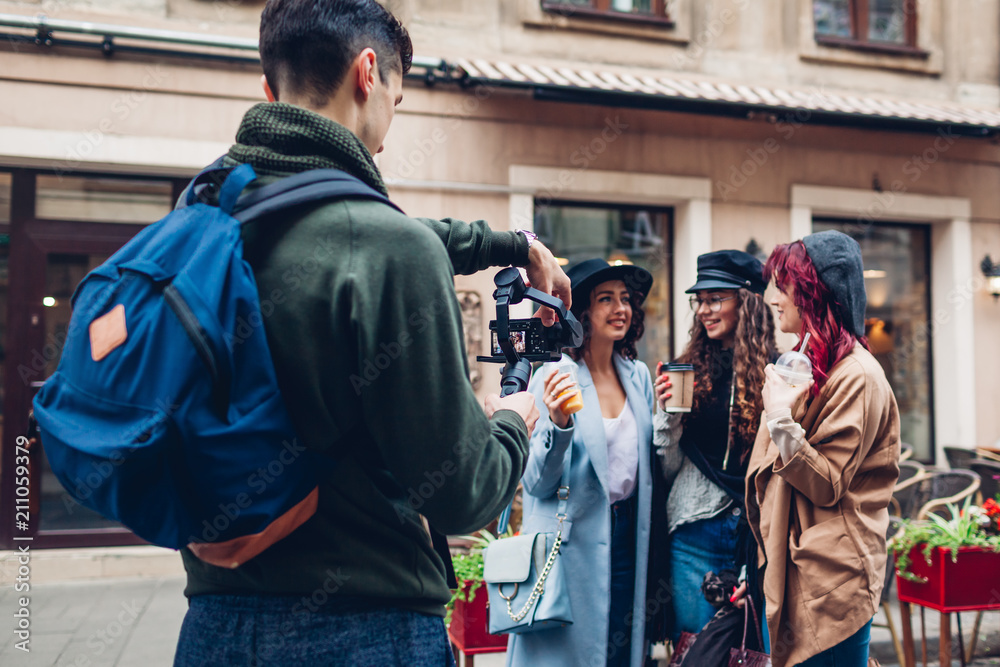 Fototapeta premium Videographer filming models on city street. Man using steadicam and camera to make footage. Video shoot