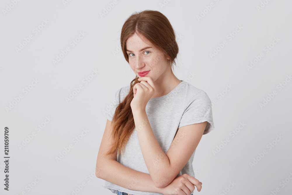 Portrait of charming happy young woman with long red hair and freckles thinking and smiling isolated over white background Looking at camera Portrait of charming happy young woman with long red hair and freckles thinking and smiling isolated over white background Looking at camera