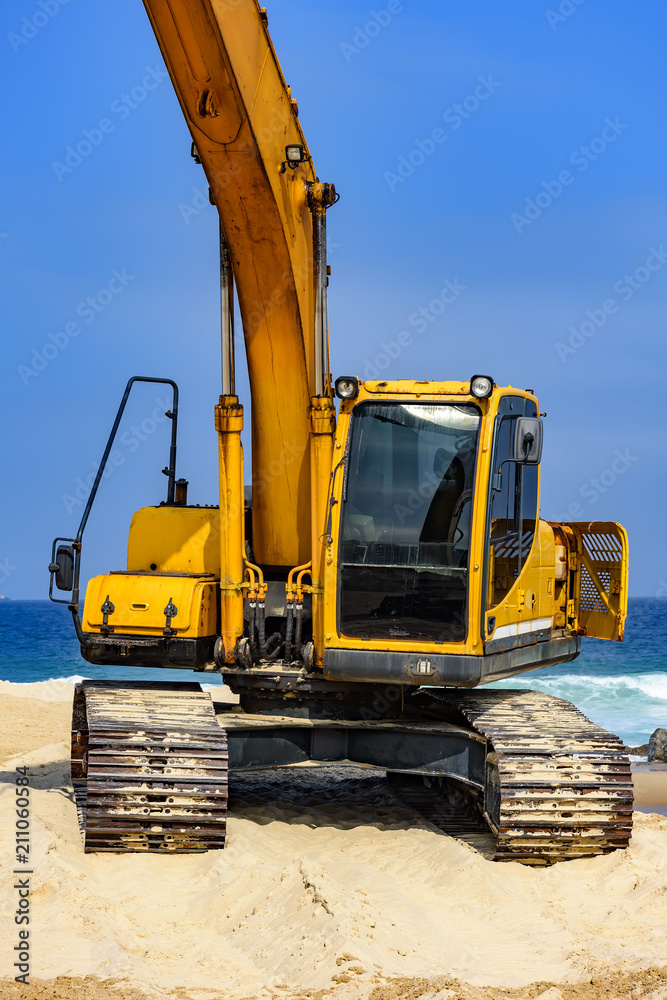 Yellow excavator cabin and arm over sand at beach in a sunny day Yellow excavator cabin and arm over sand at beach in a sunny day