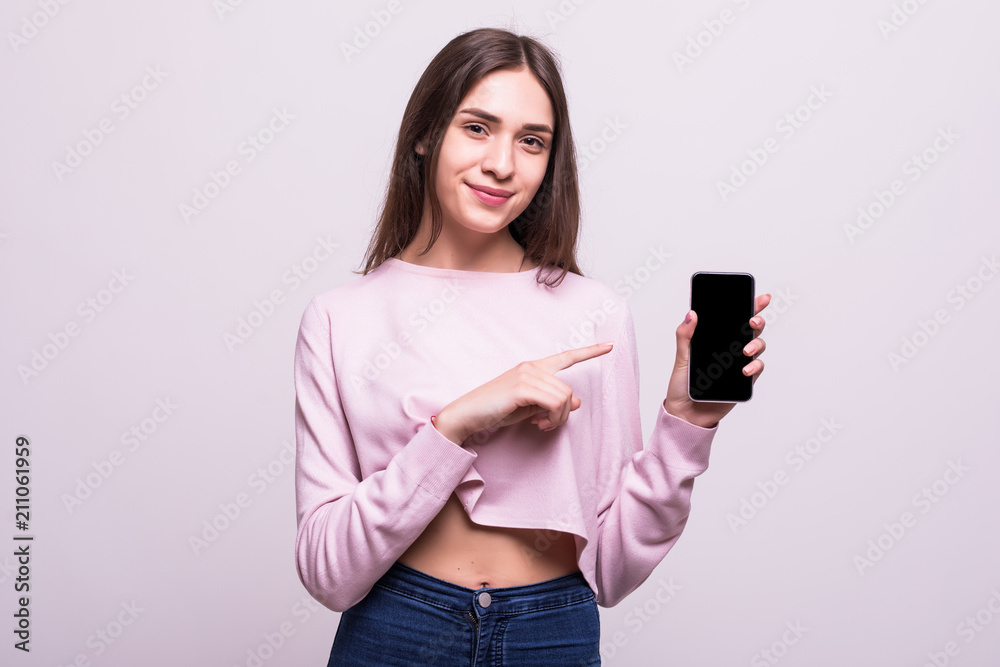 Portrait of a happy young girl pointing finger at blank screen mobile phone isolated over white background Portrait of a happy young girl pointing finger at blank screen mobile phone isolated over white background