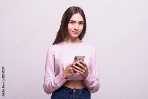 Portrait of excited cheerful lovely girl using her smartphone for typing messages to her friend, isolated on white background