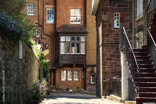 Photo of a narrow street with historical small houses, stairs and lamp in Edinburgh