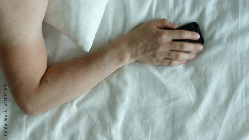 TOP VIEW: Human hand takes a phone on a bed and disable it in the morning TOP VIEW: Human hand takes a phone on a bed and disable it in the morning