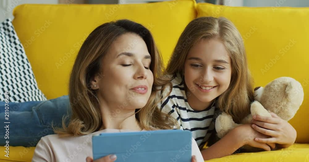Close up of the attractive woman with her teen daughter watching videon on the tablet computer and smiling. Indoors. Close up of the attractive woman with her teen daughter watching videon on the tablet computer and smiling. Indoors.