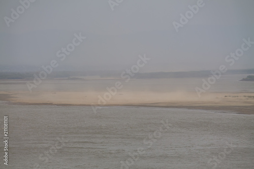 sandstorm in a river valley with green forest on the horizon seen from above