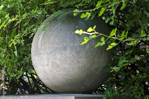 A rounds stone globe in the bushes of the forest woodland area in the summer heat.