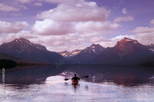 Adventurer paddling on mountain lake during morning sunrise, with beautiful scenic reflection of clouds and sky