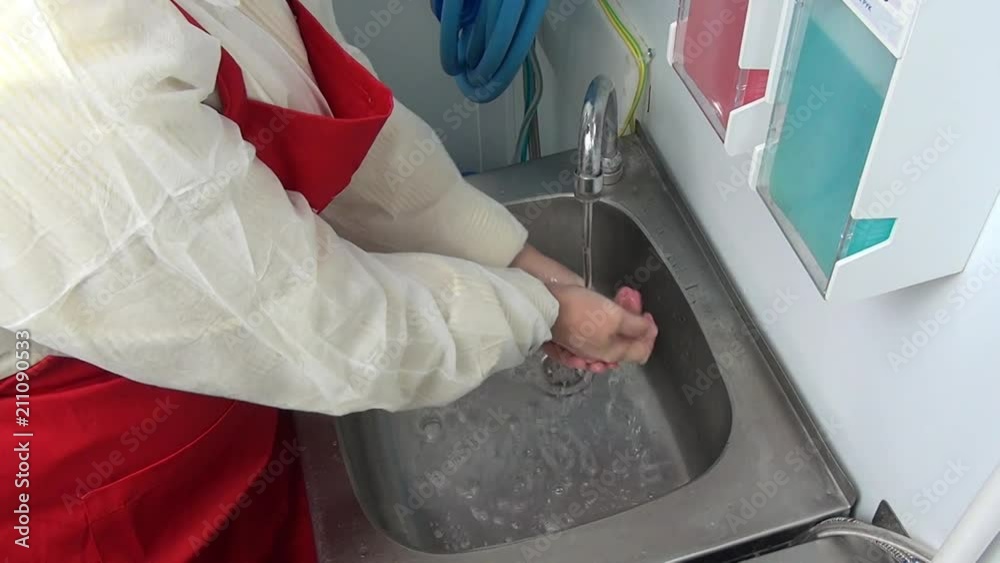 Woman worker in red apron washes her hands under the tap. Application of disinfectant solution