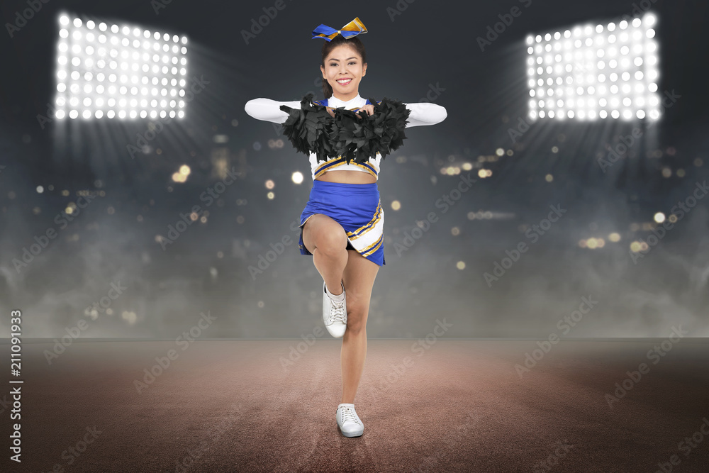 Young asian cheerleader in action with pom poms
