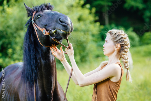 Young teenage blond girl equestrian talking with her chestnut horse. Multicolored outdoors horizontal image. photo