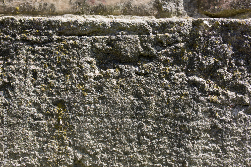 Concrete stone wall with green moss spots on it in the sunny lights. Old texture background. Concrete stone wall with green moss spots on it in the sunny lights. Old texture background.