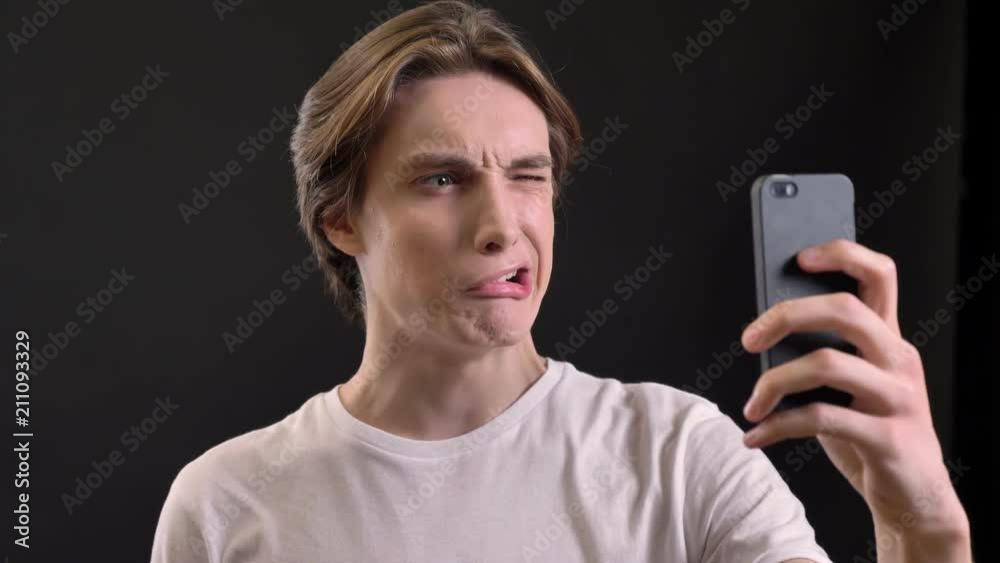 Young handsome man taking selfie and making different funny faces, isolated over black background Young handsome man taking selfie and making different funny faces, isolated over black background