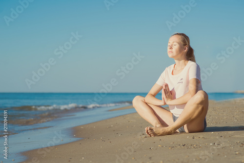 Young woman sitting on sand and doing yoga meditation on the beach