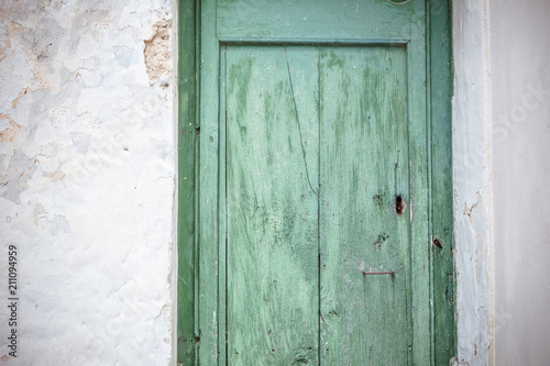 Old greenish blue wooden door and eroded white wall. Front door © Mathia