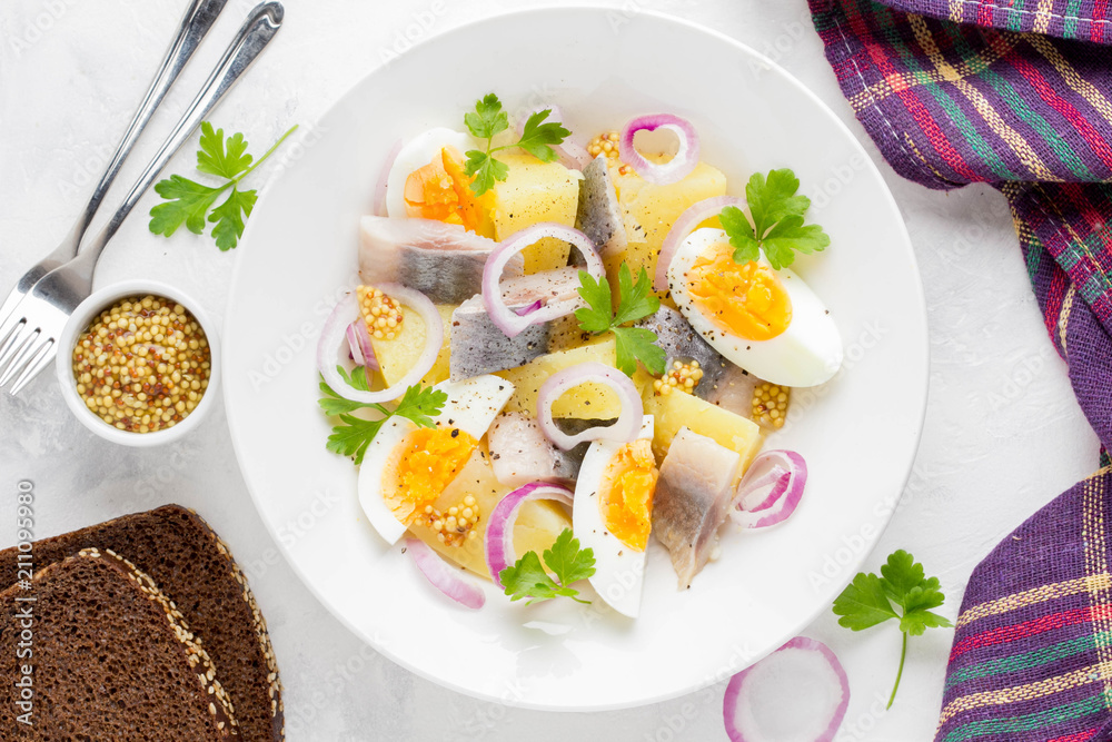 Potato salad with herring, egg, onion, tasty snack with mustard in white plate