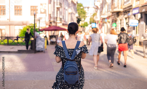 Young woman with backpack walks in summer city. Brunette woman in blue dress. © chdenisz