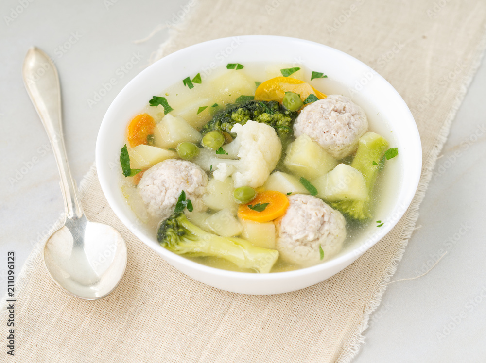 bowl of soup, a cup of broth and vegetables, meatballs made of turkey and chicken, side view bowl of soup, a cup of broth and vegetables, meatballs made of turkey and chicken, side view