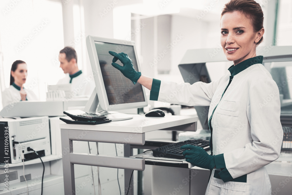 Modern hospital. Optimistic qualified doctor wearing green gloves and pointing at computer screen while expressing cheer on her face Modern hospital. Optimistic qualified doctor wearing green gloves and pointing at computer screen while expressing cheer on her face