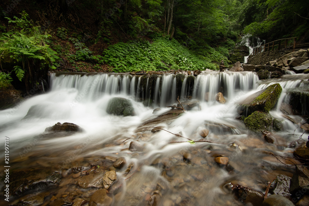 Obraz premium Beautiful mountain rainforest waterfall with fast flowing water and rocks, long exposure.