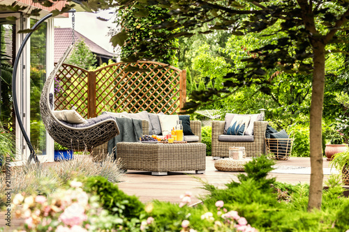 Rattan garden furniture and hanging chair on wooden terrace of house. Real photo