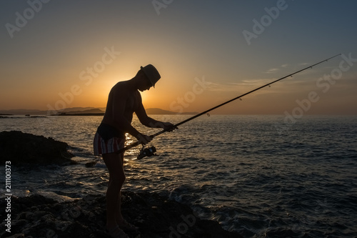 The fisherman fixes his fishing rod, evening at sunset