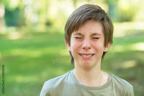 Cute handsome boy is crying outdoor. Sad early teen boy in summer park.