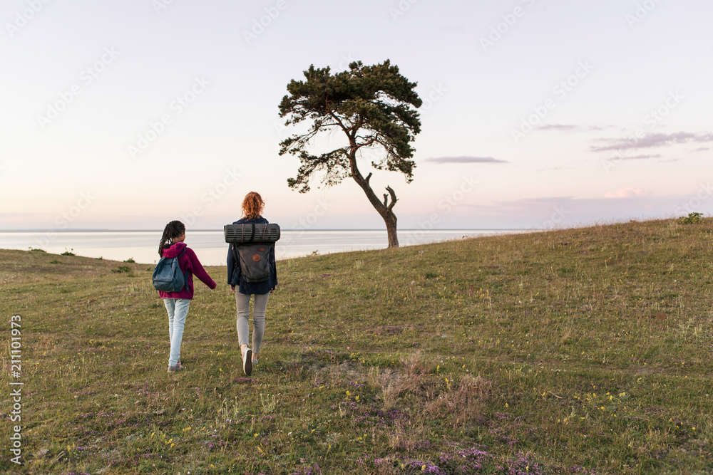 Full length rear view of mother and daughter hiking on field against sky during sunset Full length rear view of mother and daughter hiking on field against sky during sunset