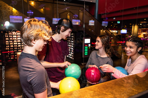 Cheerful multi-ethnic teenage friends standing with bowling balls