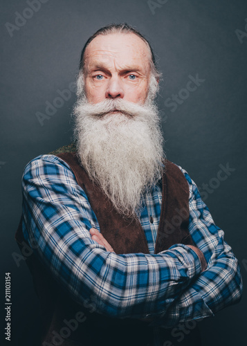 Portrait of confident bearded senior man standing arms crossed over gray background