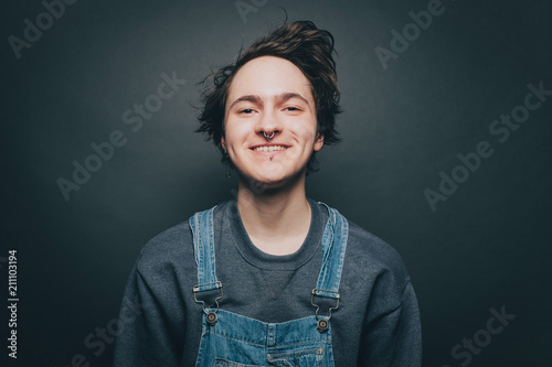 Portrait of smiling young man wearing denim overalls over gray background