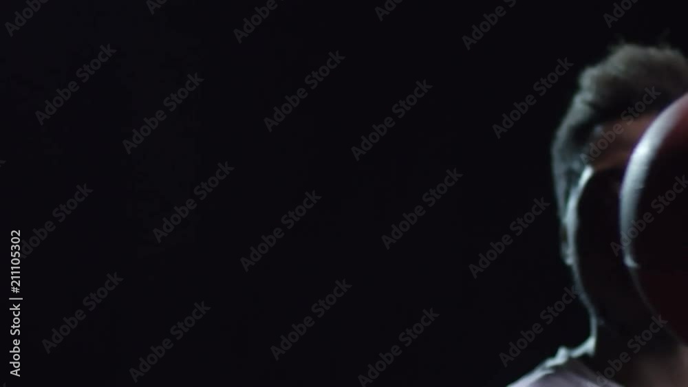 Studio shot with PAN of confident black athlete spinning basketball ball on index finger while standing isolated on dark background Studio shot with PAN of confident black athlete spinning basketball ball on index finger while standing isolated on dark background
