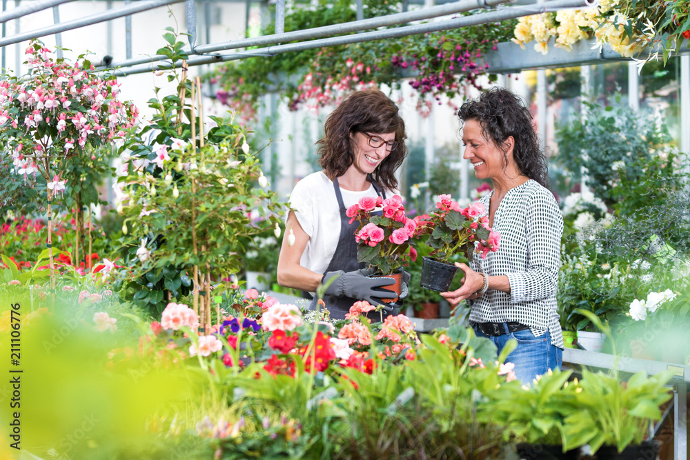 Freundliche Gärtnerin berät eine Kundin im Gewächshaus beim Blumenkauf