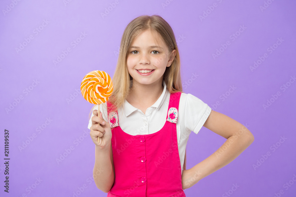 Girl smile with lollipop on violet background. Happy kid with swirl caramel on purple background. Small child smiling with candy on stick. Food and dessert. Sweet as lollipop. Diet and dieting Girl smile with lollipop on violet background. Happy kid with swirl caramel on purple background. Small child smiling with candy on stick. Food and dessert. Sweet as lollipop. Diet and dieting