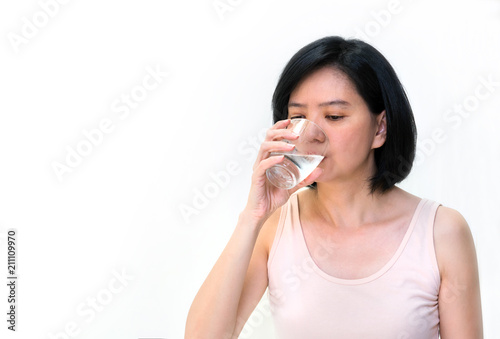 Beautiful Asian woman with clean skin, natural make-up drinking cold water isolated on white background. Young  woman in studio holding glass in her hand. Image for skin and healthy concept,copy space