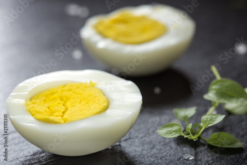 Slices of boiled hard eggs on a dark slate with green oregano