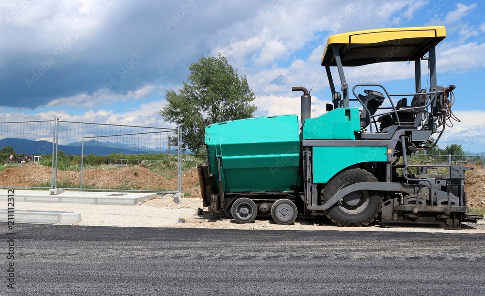 Asphalt paver vehicle on the edge of a newly paved road in a new urban development construction site