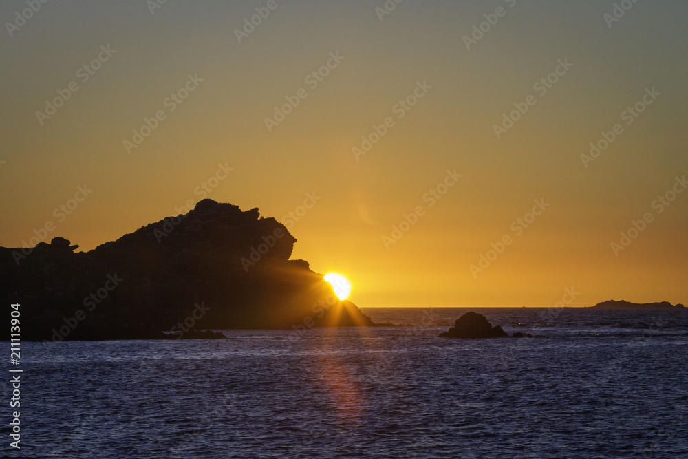 Coucher de soleil sur la mer derrière un rocher