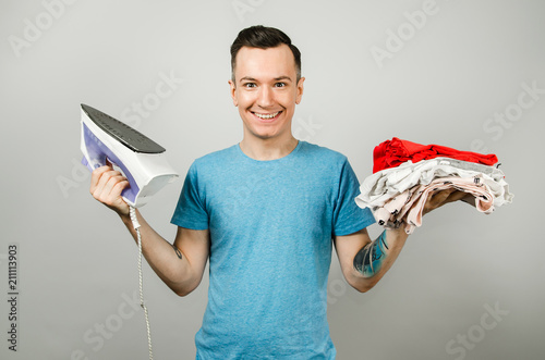 Young gyu holds iron and keeps a stack of laundry on a light gray background. photo