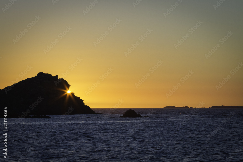 Coucher de soleil en mer derrière un rocher