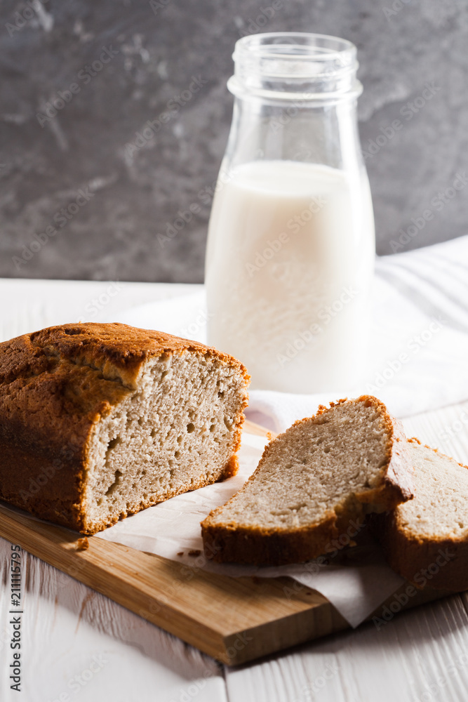 Banana bread in a pan with white parchment paper on a white wooden table with milk bottle in the background. Close up. Bakery concept