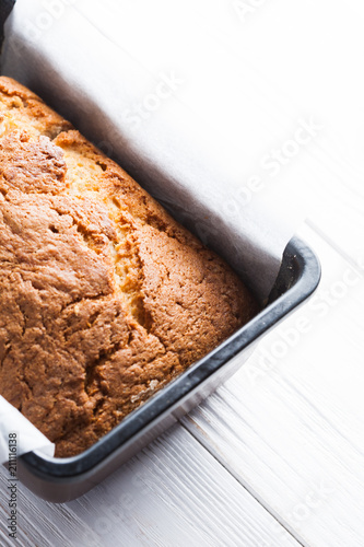 Banana bread in a pan with white parchment paper on a white wooden table. Close up. Bread cracks pattern. Bakery concept