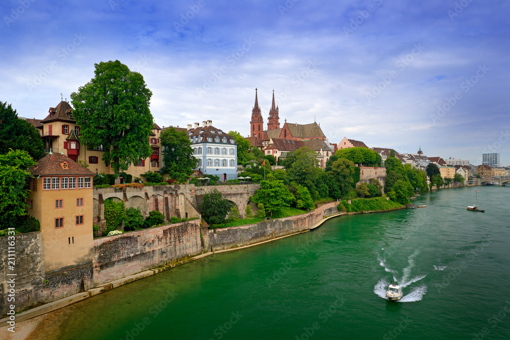Basel with red stone Munster cathedral and the Rhine river, Switzerland, Europe. View of the Old Town of Besel. City centre with green trees during summer, boat in the water.