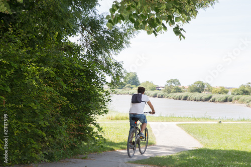 Fototapeta Naklejka Na Ścianę i Meble -  man riding a bicycle on the bike path next to the river during holidays