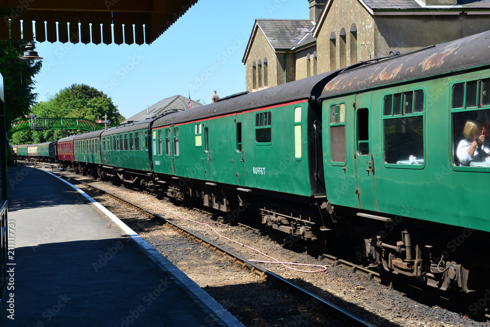 Fototapeta premium A steam train pulling coaches waiting to depart from a station.